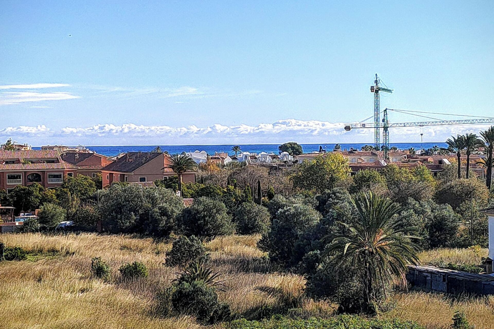 Un quartier résidentiel situé sur la côte, avec des maisons, une grue de construction et une chaîne de montagnes en arrière-plan.