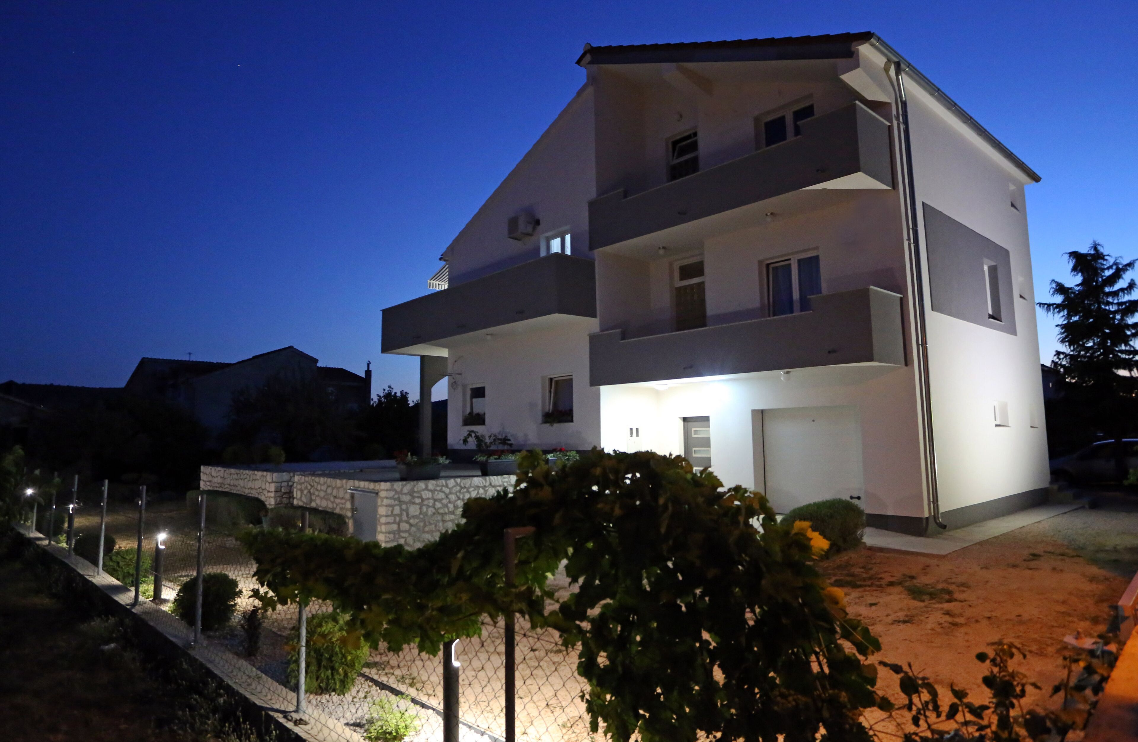 A multi-story residential building with balconies, a stone wall, and a well-lit entrance.