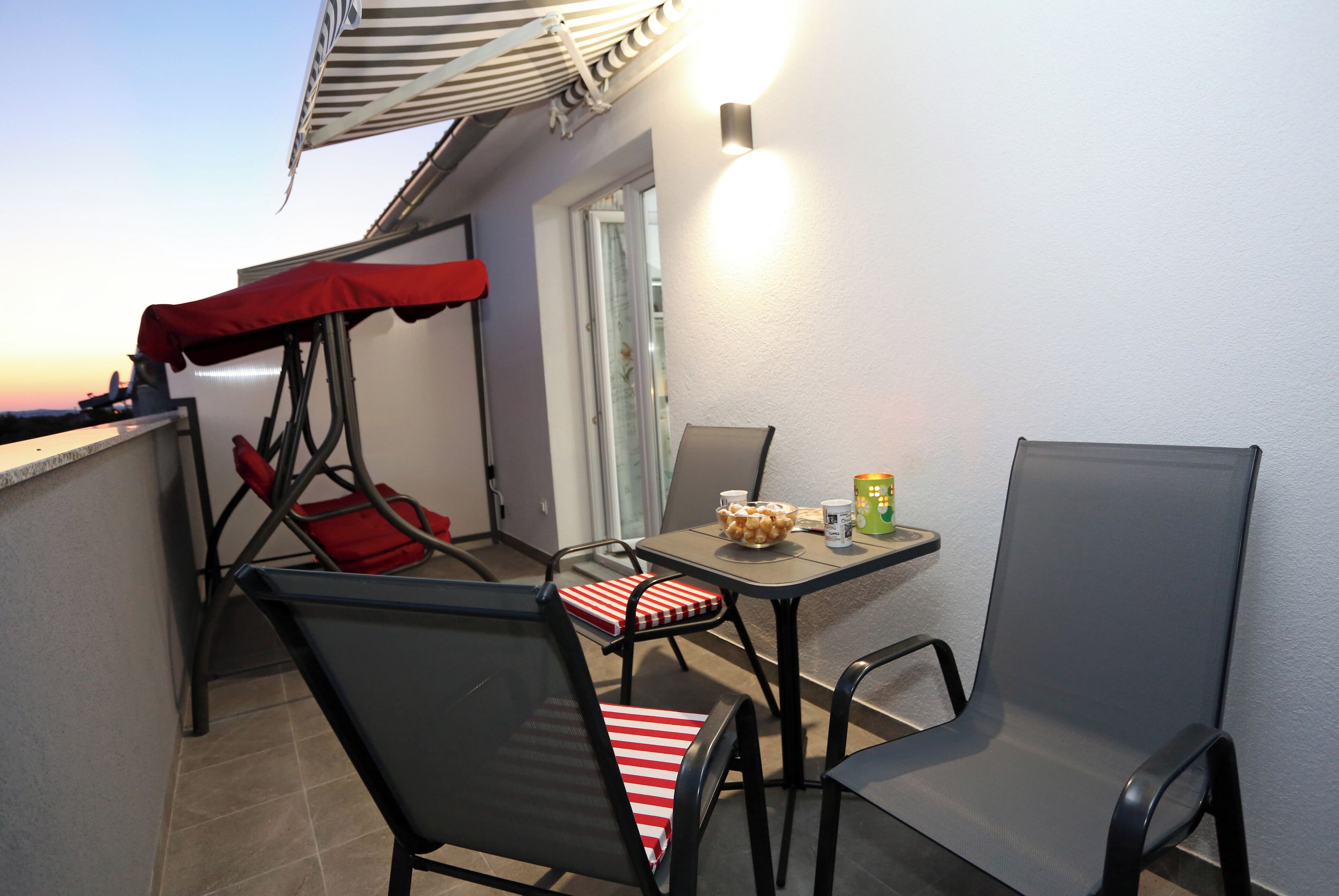 A balcony with a table, chairs, and a red canopy.