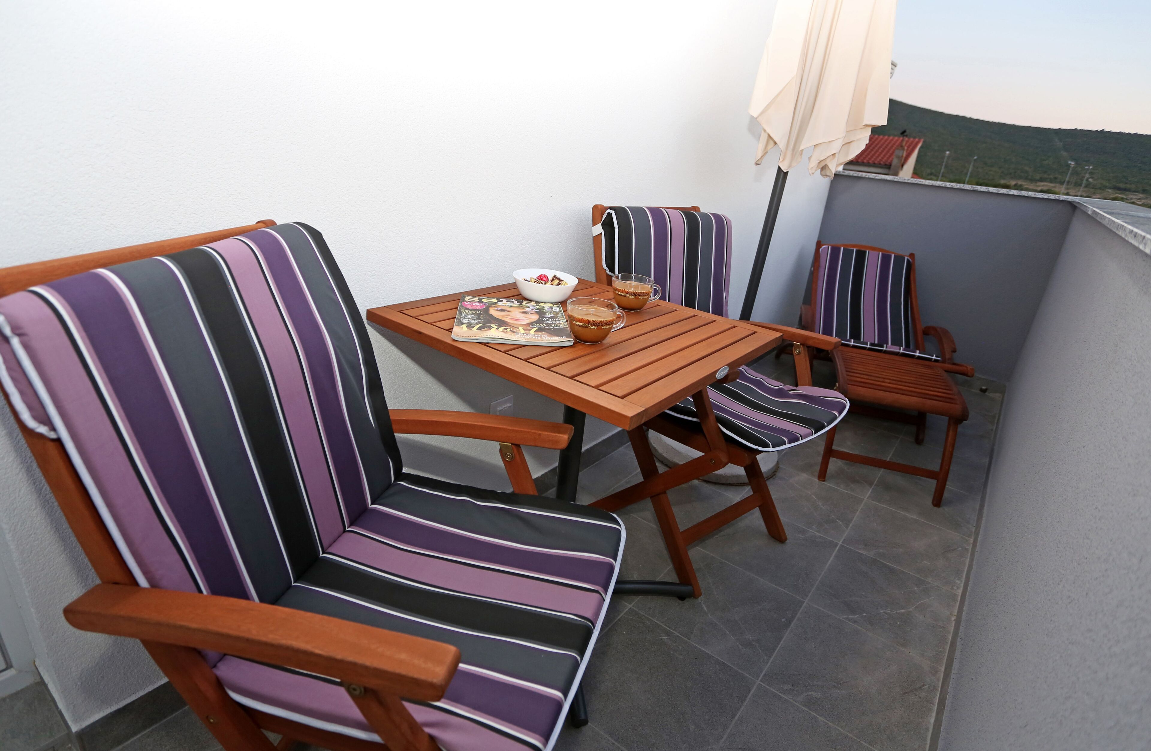 A balcony with striped chairs, a wooden table, and a bowl of cereal.