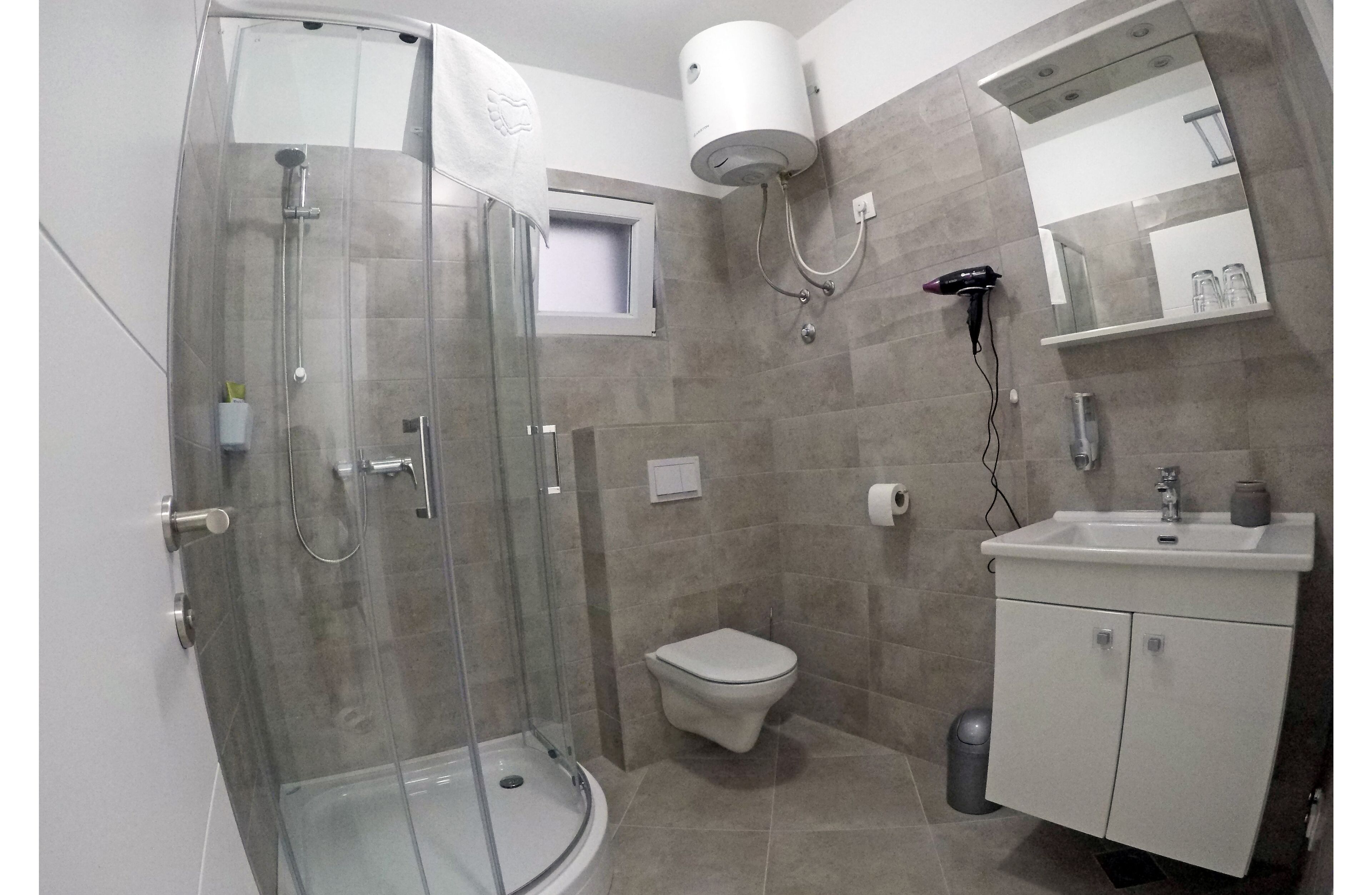 Un baño con ducha de vidrio, inodoro, lavamanos con espejo y un perchero para toallas.