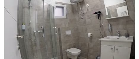 Ein Badezimmer mit Duschkabine, Toilette, Waschbecken mit Spiegel und Handtuchhalter.