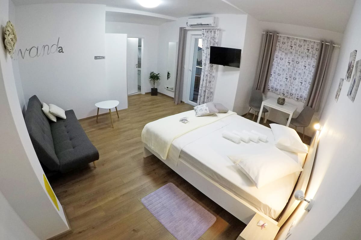 A modern bedroom with a bed, a sofa, a small table, and a TV.
