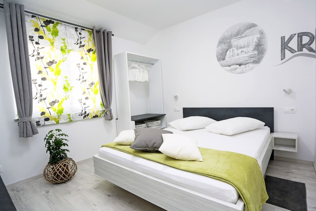 A modern bedroom with a bed, bedside tables, a wardrobe, a window with curtains, and a wall with a logo.