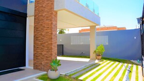 Una casa moderna con una puerta de garaje negra, un pilar de ladrillo y un pequeño jardín con un camino a rayas.