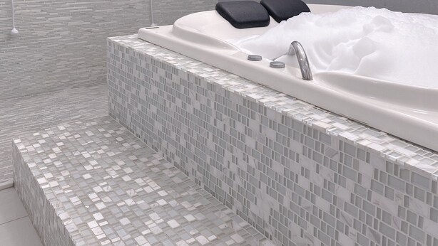 Un baño moderno con cabina de ducha revestida de azulejos de vidrio, una bañera independiente y un lavabo blanco.