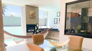 Un comedor moderno con mesa de vidrio, sillas acolchadas, una hamaca y una zona de cocina con barra.