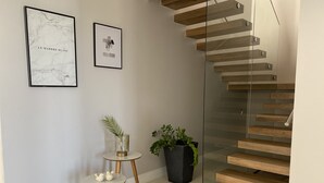 Un interior moderno con una escalera, dos obras de arte enmarcadas, una pequeña mesa redonda con una planta, y otra planta en maceta junto a la mesa.