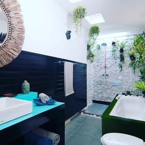 A modern bathroom with a black vanity, a white sink, a green bathtub, and a shower area with plants. - Villa Udjung (Seminyak)
