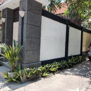A building with a white exterior wall and a black baseboard. There are plants along the baseboard and a concrete planter with green foliage. - Villa Udjung (Seminyak)