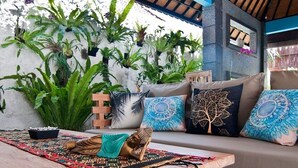 A cozy outdoor seating area with a wooden table, cushions, and a variety of potted plants.