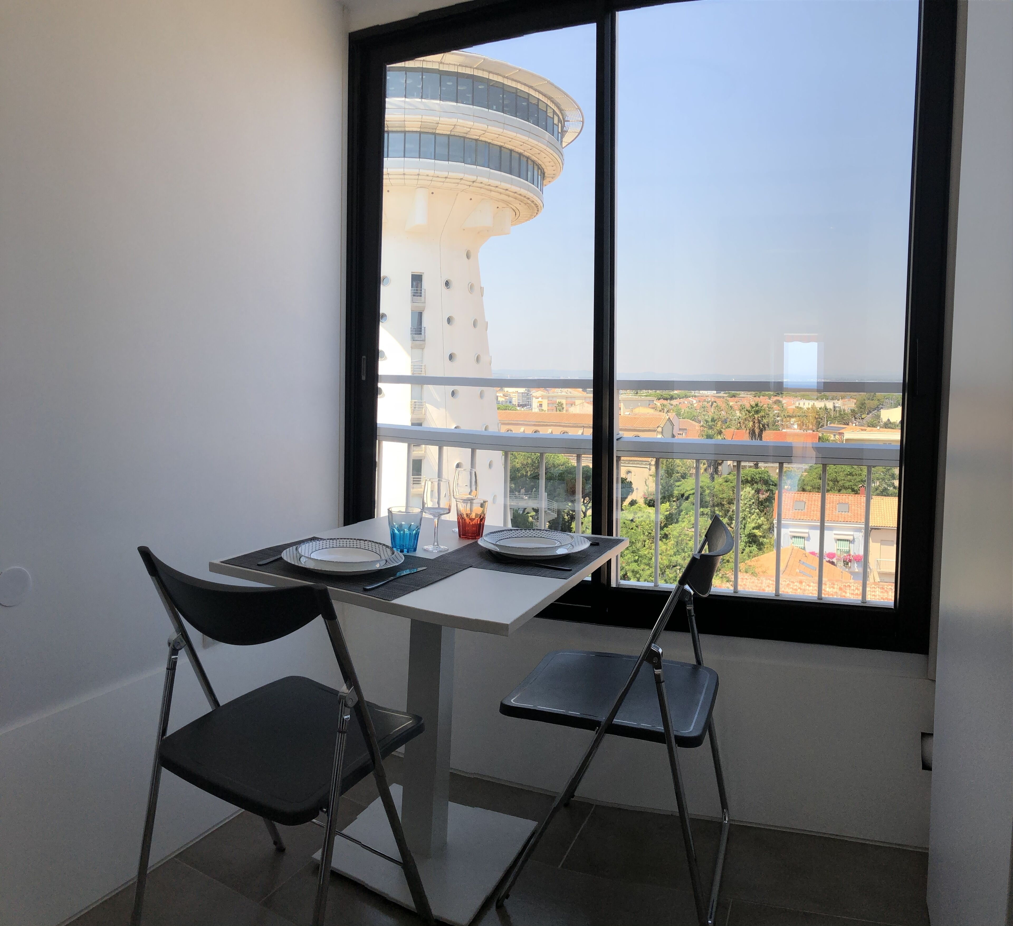 A balcony with a table set for two, two chairs, and a view of a modern building and surrounding area.