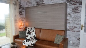 A cozy room with a brown leather sofa, a wooden side table, and a brick wall.