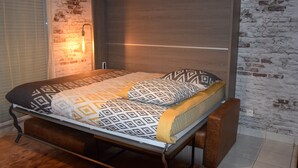 A bed with a patterned bedspread and pillows, a wooden headboard, and a wall with exposed brick.
