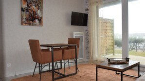 A modern living room with a dining table, chairs, a flat-screen TV, and a large window with a view.