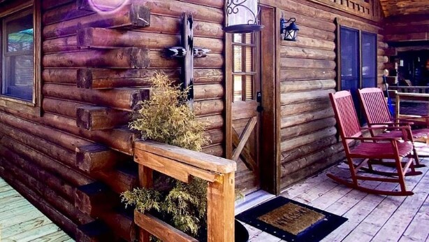 Un rustico chalet in legno con veranda e terrazza, un portico con poltrone a dondolo e una lanterna.