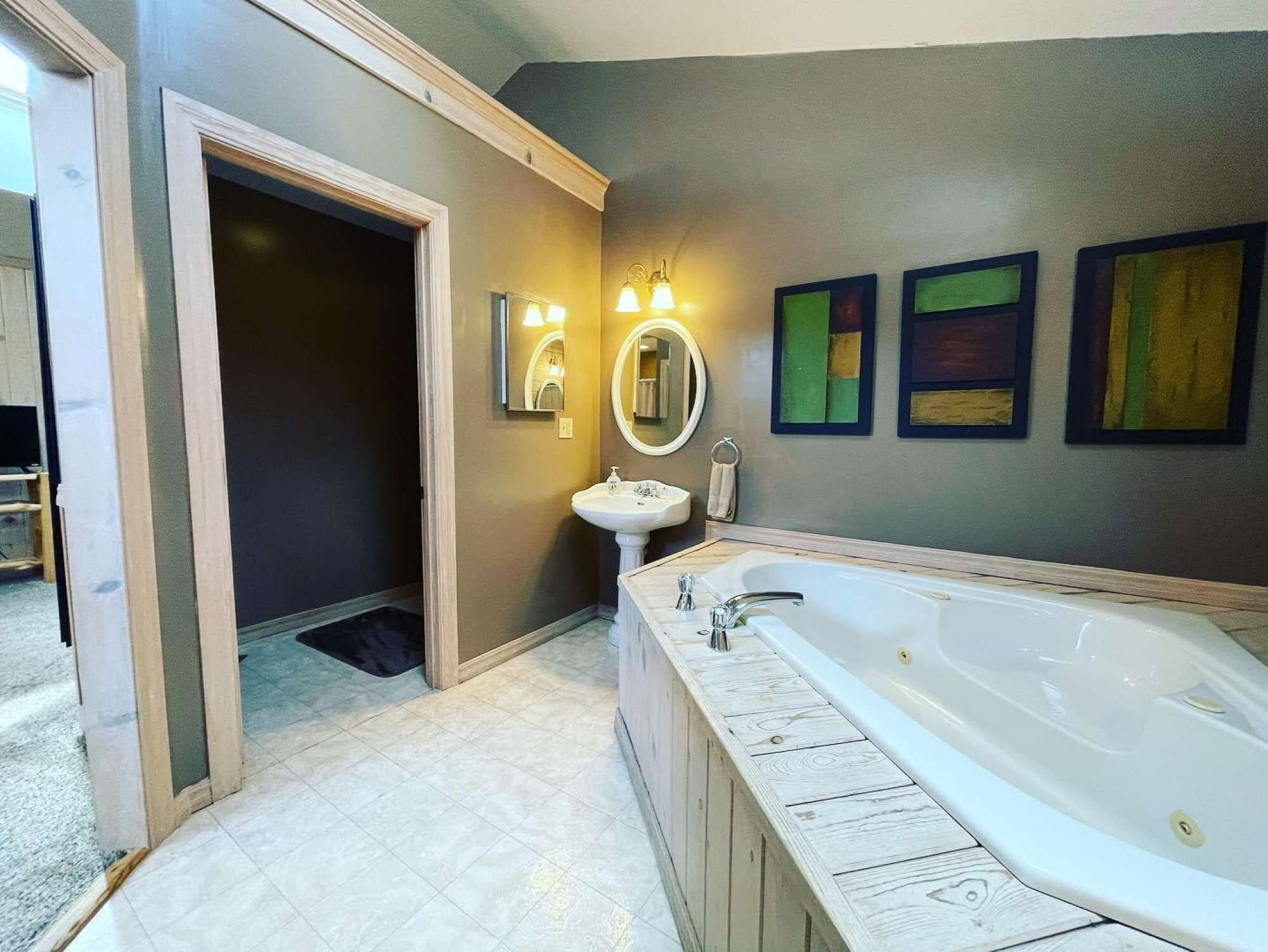 A bathroom with a large bathtub, a sink, and a mirror. There are three framed artworks on the wall.
