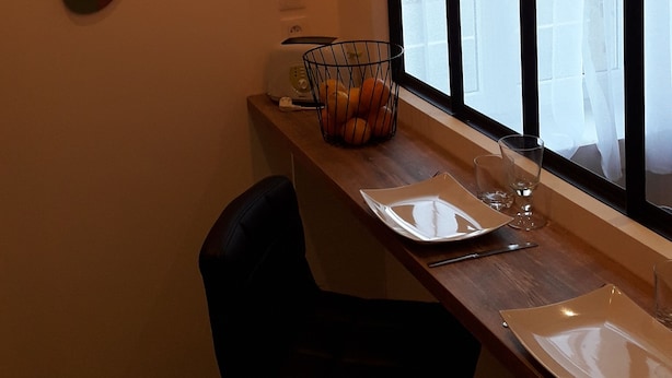 Un comedor con mesa de madera, dos sillas, una ventana con cortinas traslúcidas y dos lámparas colgantes.