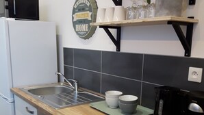 Una cocina moderna con encimera de madera, lavamanos de acero inoxidable y lavavajillas empotrado. Hay estantes sobre la encimera con tazas y una planta en maceta.