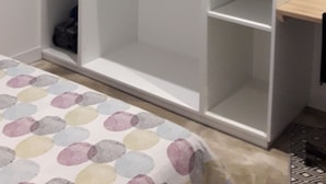 Un armario blanco con varios estantes y espacio para colgar, un estante pequeño en la parte inferior, y una puerta con manija.