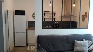 Cocina compacta con refrigerador, microondas y pileta. Se observa un sofá con un cojín estampado en primer plano.