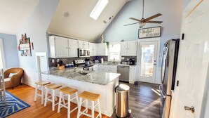 A modern kitchen with white cabinets, a granite countertop, and a central island with bar stools. - June 27-July 4th is OPEN. CHECK THE DISCOUNTED RATES. (Corolla)