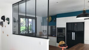 A modern kitchen with a large window, a wooden dining table, and a black refrigerator. - House the Horsemen (Anglet)