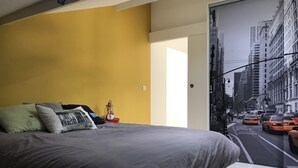A modern bedroom with a large bed, a yellow wall, and a cityscape view through a window. - House the Horsemen (Anglet)