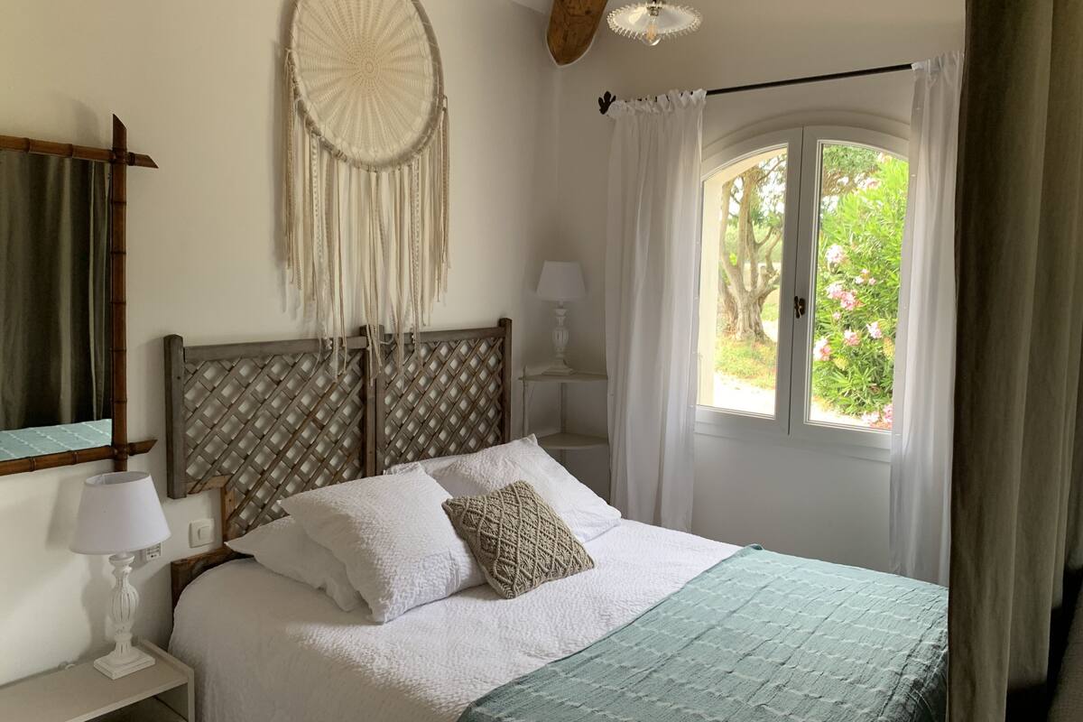 A bedroom with a bed, a nightstand, a lamp, a dreamcatcher, and a window with curtains.