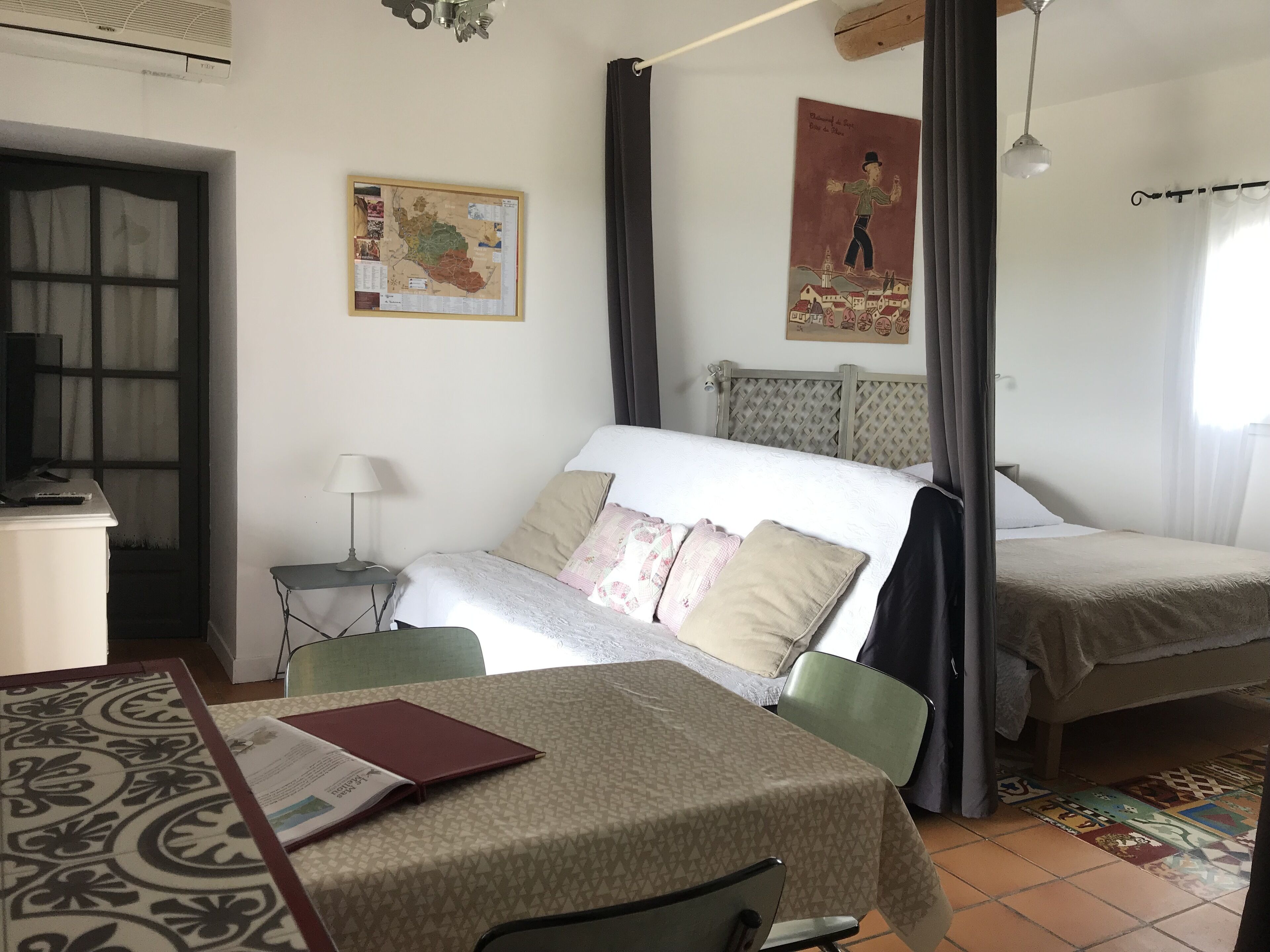 Una habitació d'hotel amb un llit, un escriptori amb una cadira, una taula amb una cadira, un mapa a la paret i un quadre.