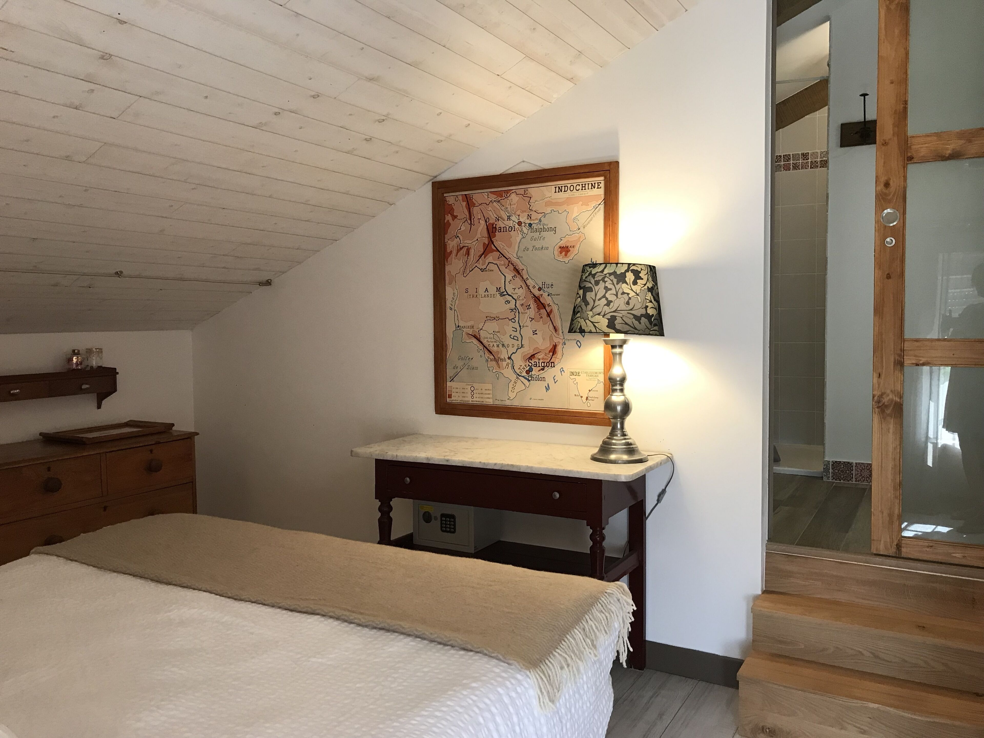 Une chambre à coucher avec un lit, une table de chevet en bois, une carte accrochée au mur et une lampe.