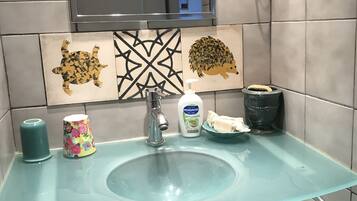 Une salle de bain avec un lavabo en verre, un miroir, un sèche-cheveux et des carreaux décoratifs.