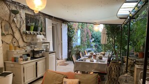 A cozy outdoor dining area with a table set for two, surrounded by potted plants and a rustic stone wall. - Le Mas Mellou (Orange)