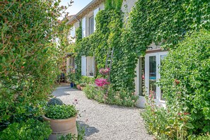 A garden pathway leading to a building with a white facade and windows. - Le Mas Mellou (Orange)