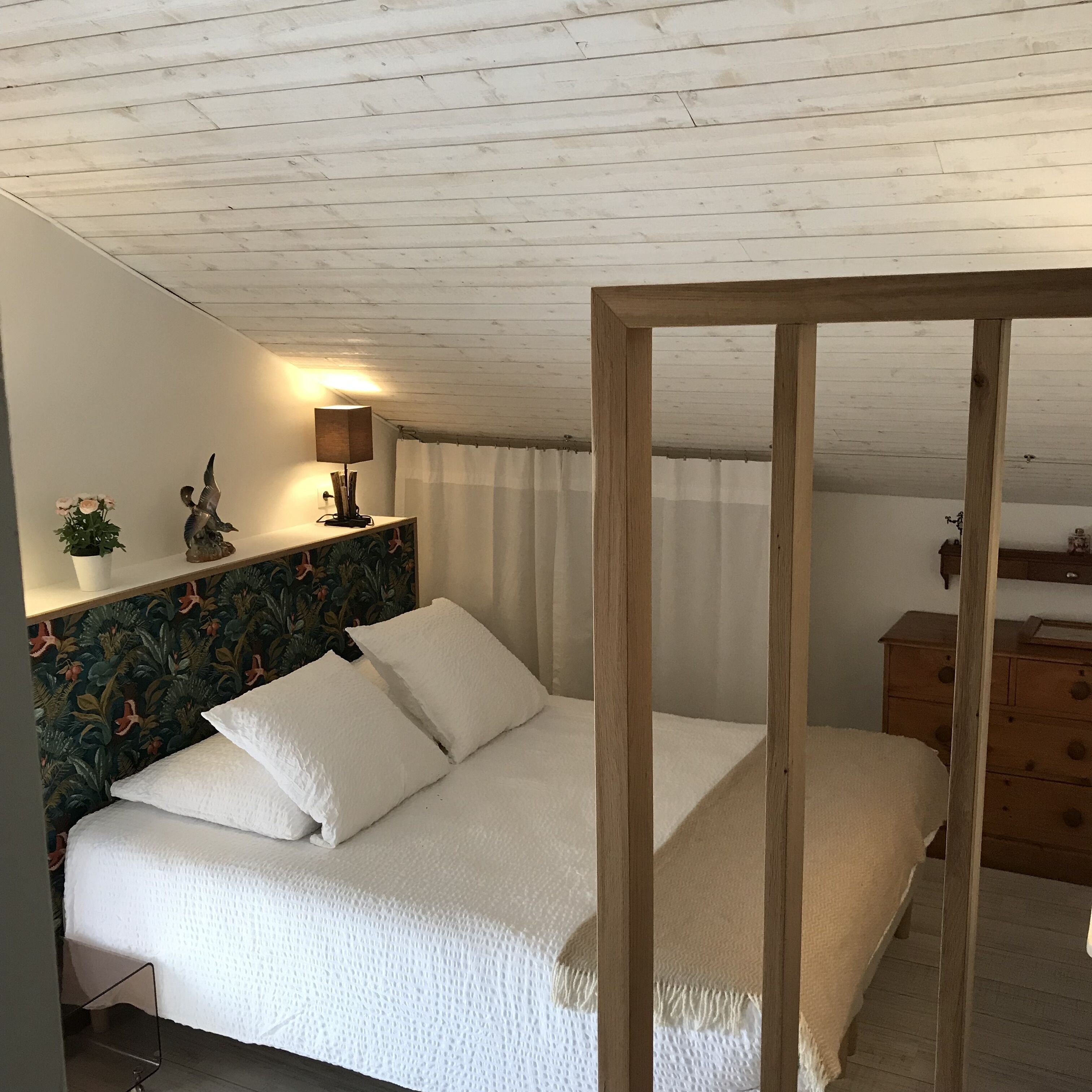 A bedroom with a wooden headboard, a bed with white bedding, a nightstand with a lamp, and a dresser.