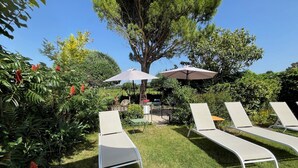 A garden with three white lounge chairs and two umbrellas. - Le Mas Mellou (Orange)