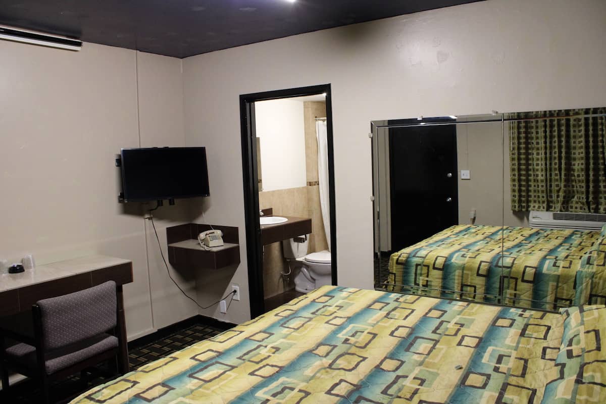 A hotel room with a bed, a desk, a chair, a television, a bathroom with a toilet and sink, and a door leading to another room.