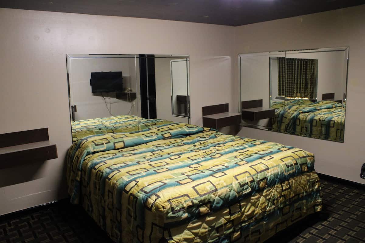 A hotel room with a bed, two bedside tables, a TV mounted on the wall, and a large mirror.