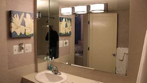 A bathroom with a large mirror, a sink, and two wall-mounted light fixtures. - Royal Budget Inn (Redford)
