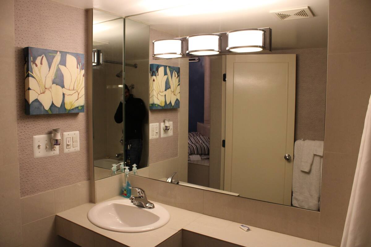 A bathroom with a large mirror, a sink, and two wall-mounted light fixtures.