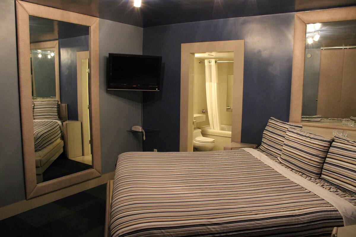 A hotel room with a bed, a television, a mirror, and a bathroom visible through an open door.