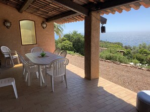 Un patio couvert avec une table et des chaises, une vue sur la mer et une pergola.