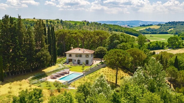 A large house with a swimming pool, surrounded by lush greenery and hills.