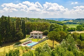 A large house with a swimming pool, surrounded by lush greenery and hills.