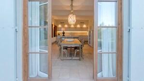 An open dining area with a central table and chairs, a hanging light fixture, and a kitchen in the background.