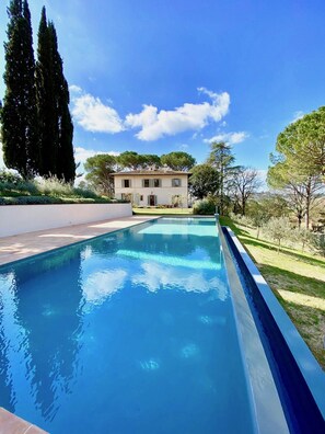 A swimming pool with a clear blue water surface, surrounded by a well-maintained lawn and tall trees.