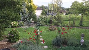 A garden with a variety of plants, a small pond, and a decorative metal archway. - With us (Tittling)