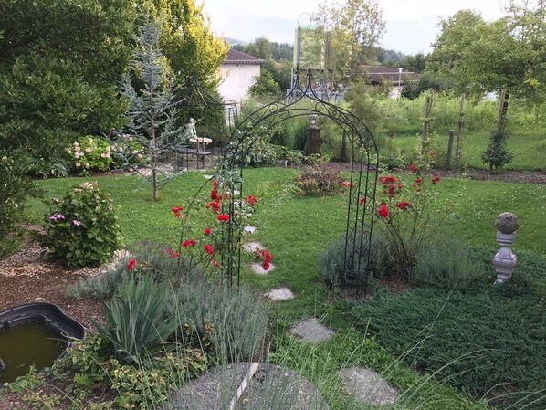 Un jardin agrémenté de diverses plantes, d’un petit étang et d’une arche décorative en métal.