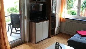 A compact living space with a kitchenette, a sofa, a coffee table, and a sliding glass door leading to an outdoor area. - With us (Tittling)