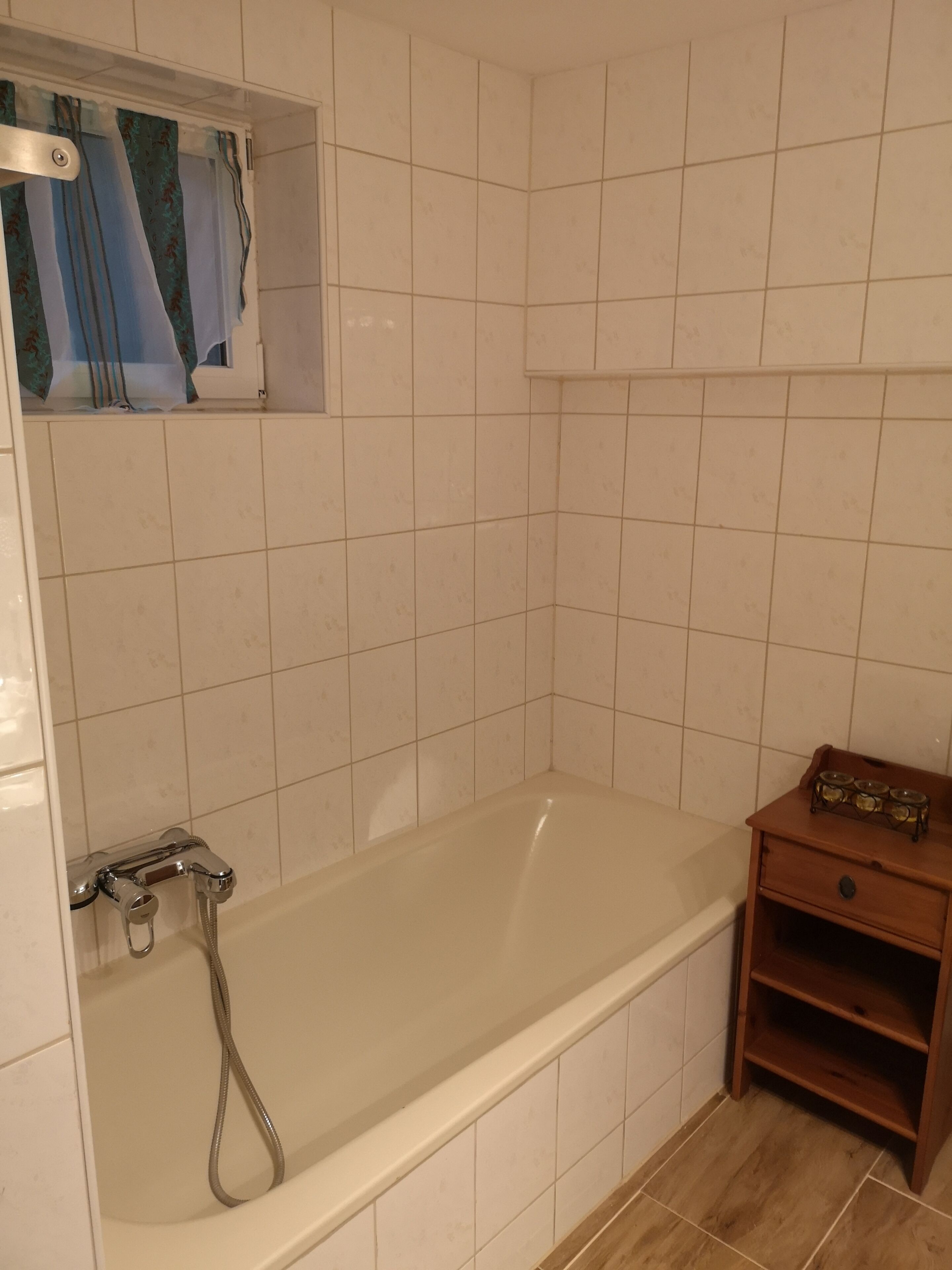 Une salle de bain avec une baignoire, une douche et une petite étagère en bois sur laquelle se trouve un plateau.